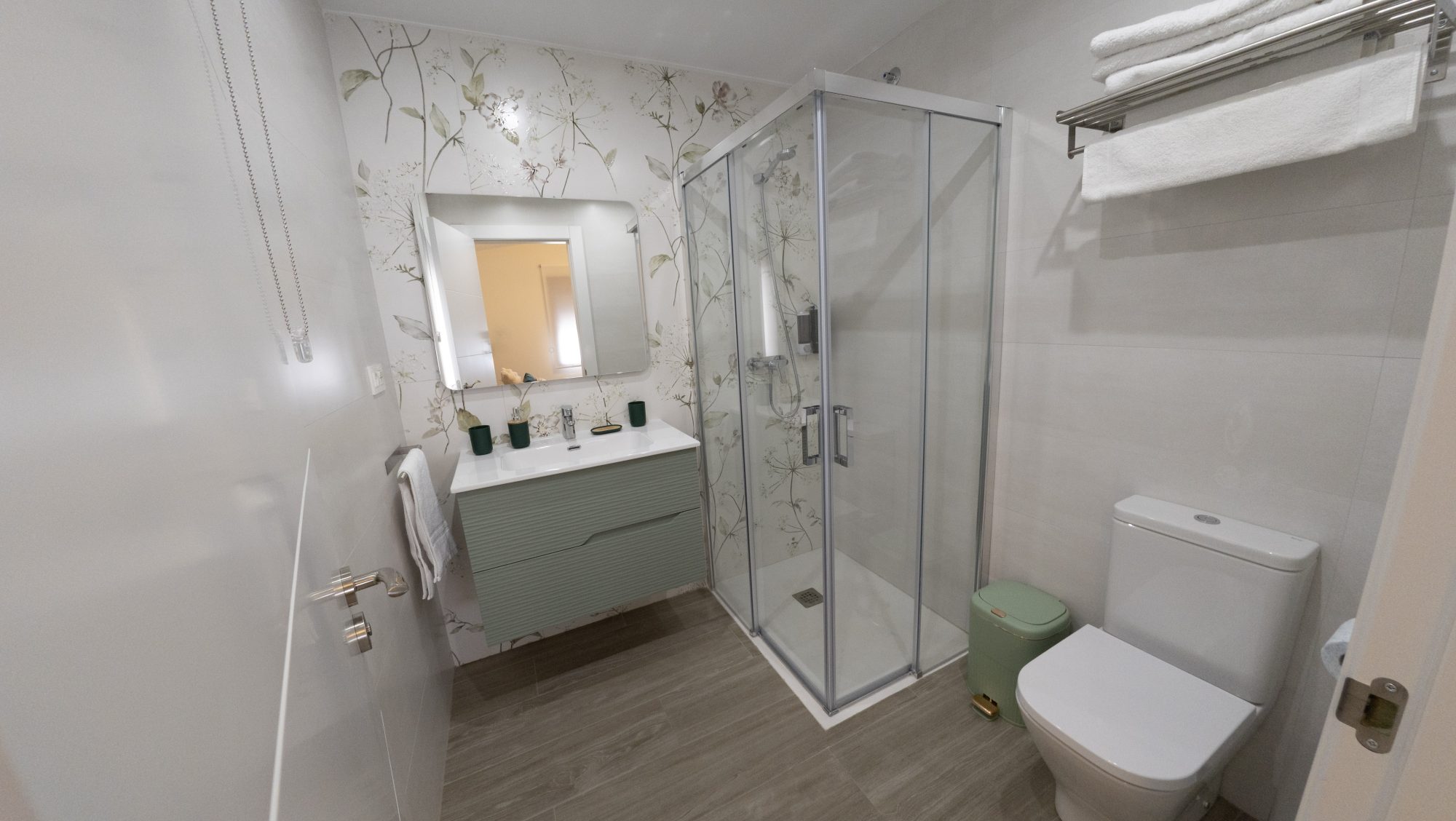Baño botánico con papel pintado floral, mueble de lavabo en verde salvia y ducha de cristal.